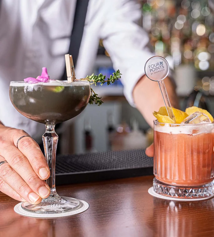 Barista che serve due cocktail colorati al bancone del bar