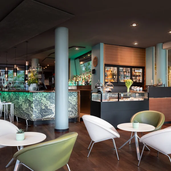 Modernes Barinterieur mit weißen und grünen Stühlen und beleuchtetem Tresen