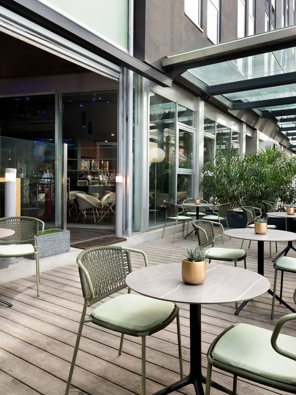 Überdachte Terrasse mit runden Tischen und grünen Stühlen